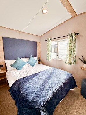 A bedroom with a bed, a headboard, a window with curtains, and a ceiling light. - The Retreat - A Luxurious Caravan in Towyn, Wales (Towyn)