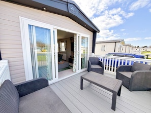 A covered outdoor deck with wicker furniture and a sliding glass door leading to an interior space. - The Retreat - A Luxurious Caravan in Towyn, Wales (Towyn)