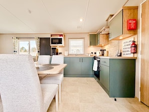 A compact kitchen with a microwave, stove, and cabinets. There is a dining table with chairs and a window with curtains.