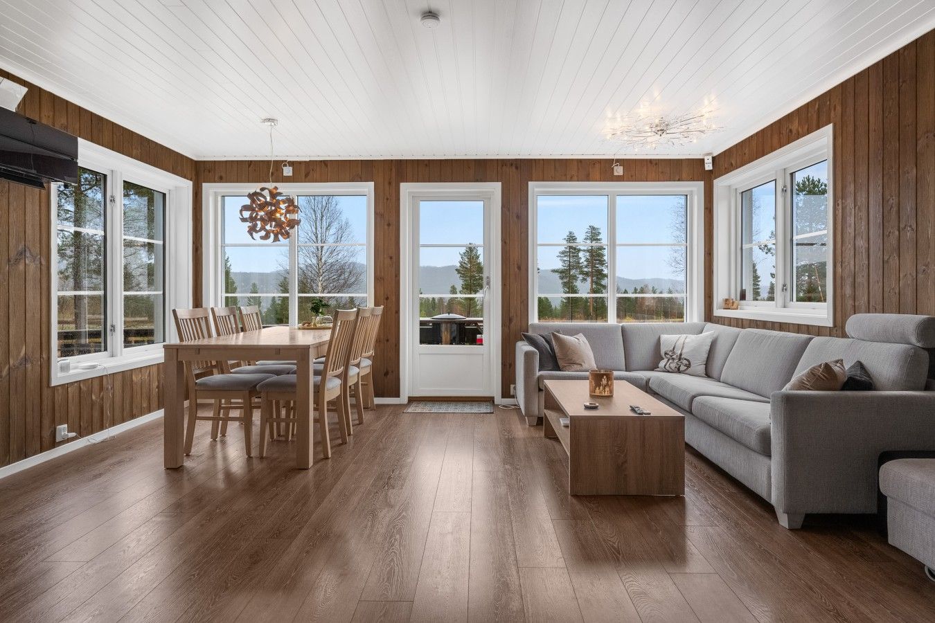 A spacious living room with a wooden floor, a dining area with a table and chairs, and a grey sofa.