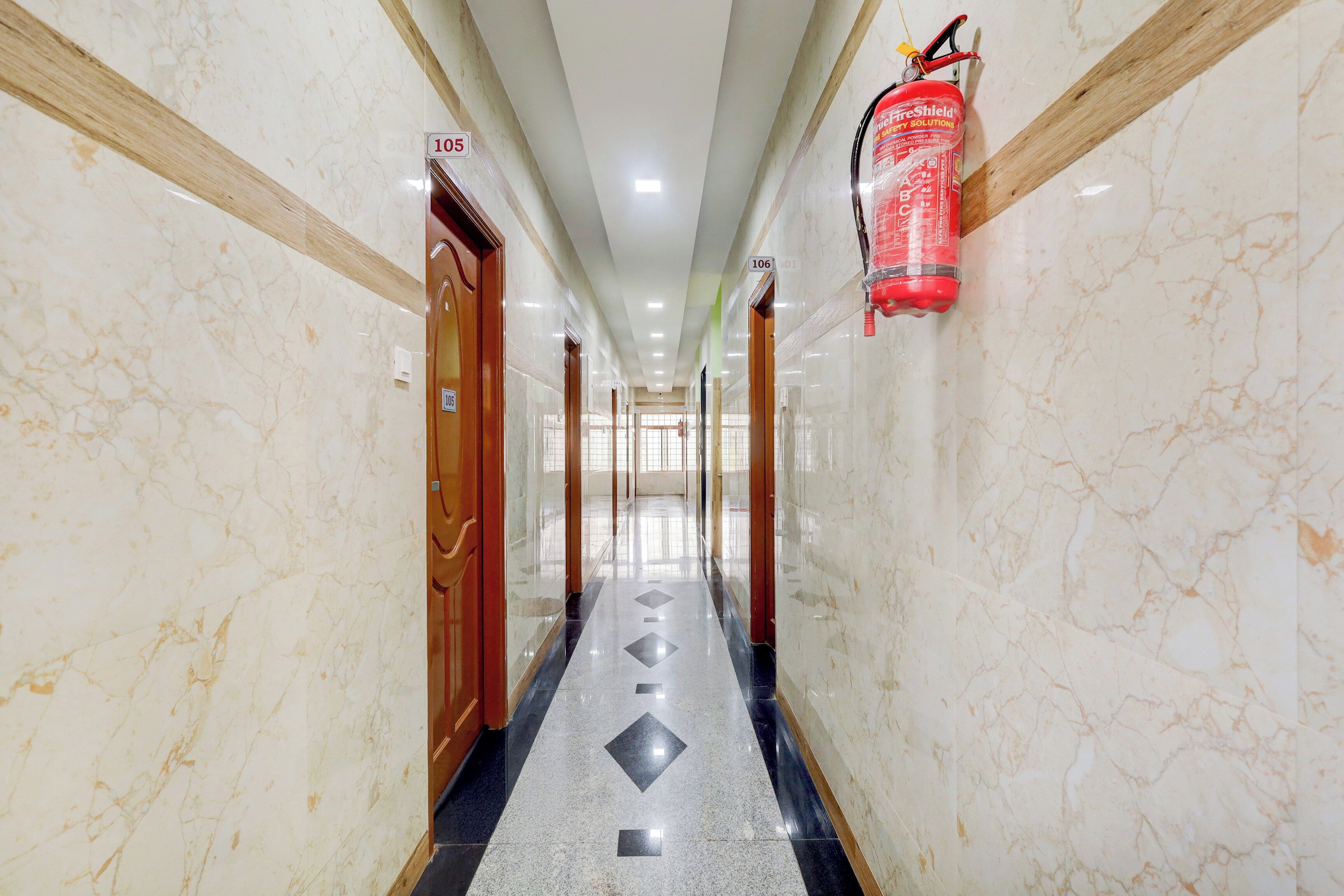 Un pasillo con paredes de mármol, puertas numeradas y un extintor de incendios en la pared.