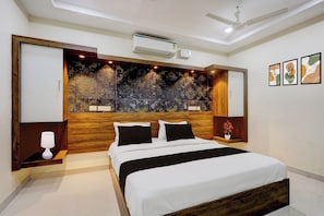 Une chambre moderne avec une tête de lit en bois, un lit avec une literie blanche, une table de chevet avec une lampe et un ventilateur de plafond.