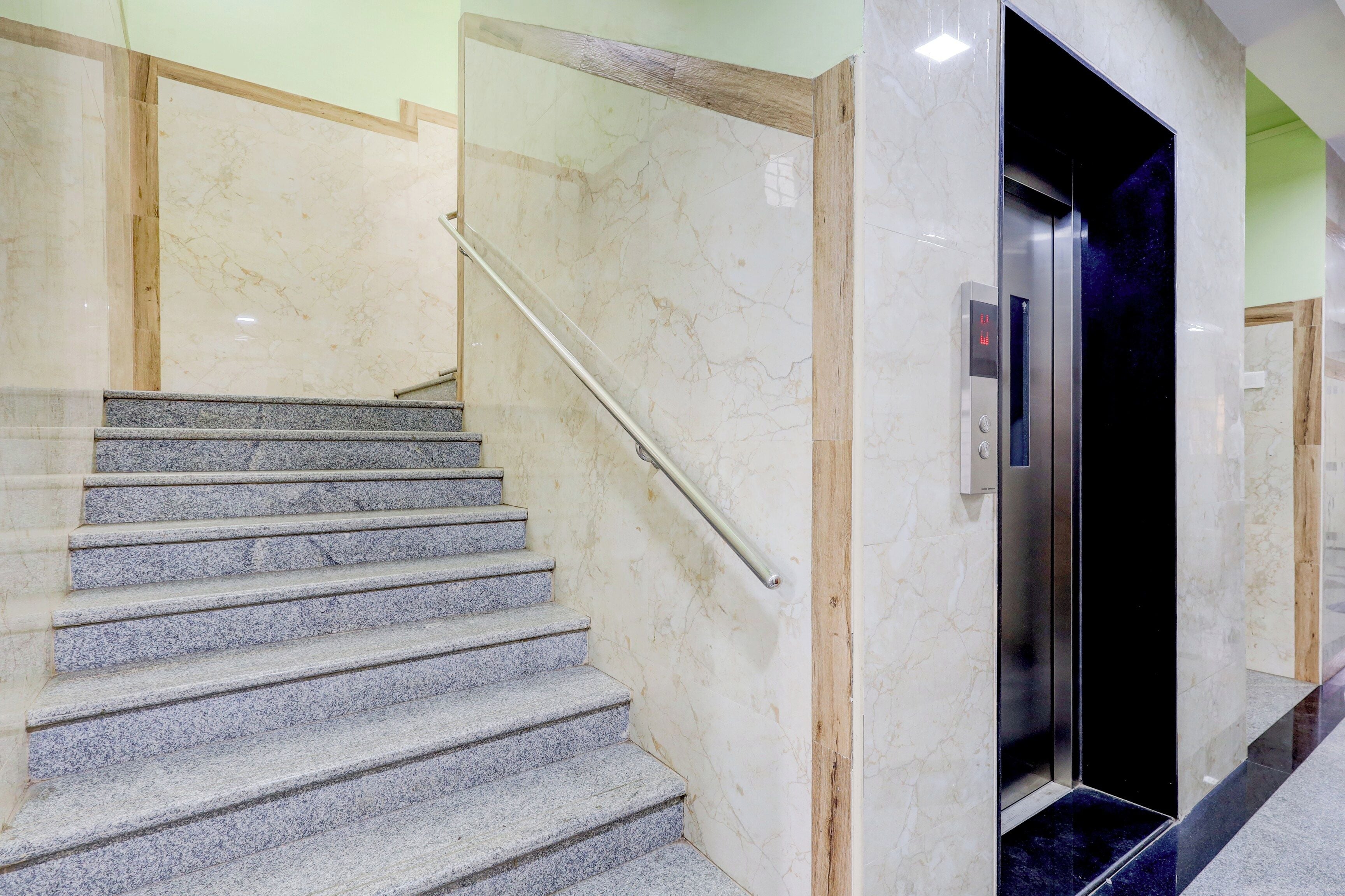 Una escalera con paredes de mármol y barandilla de metal que conduce a una puerta con pantalla digital.