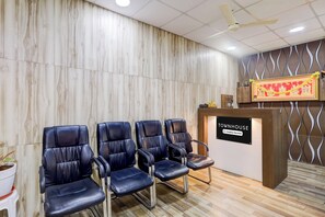 Un espace d’accueil avec un mur en bois, un comptoir de réception et quatre fauteuils en cuir noir.