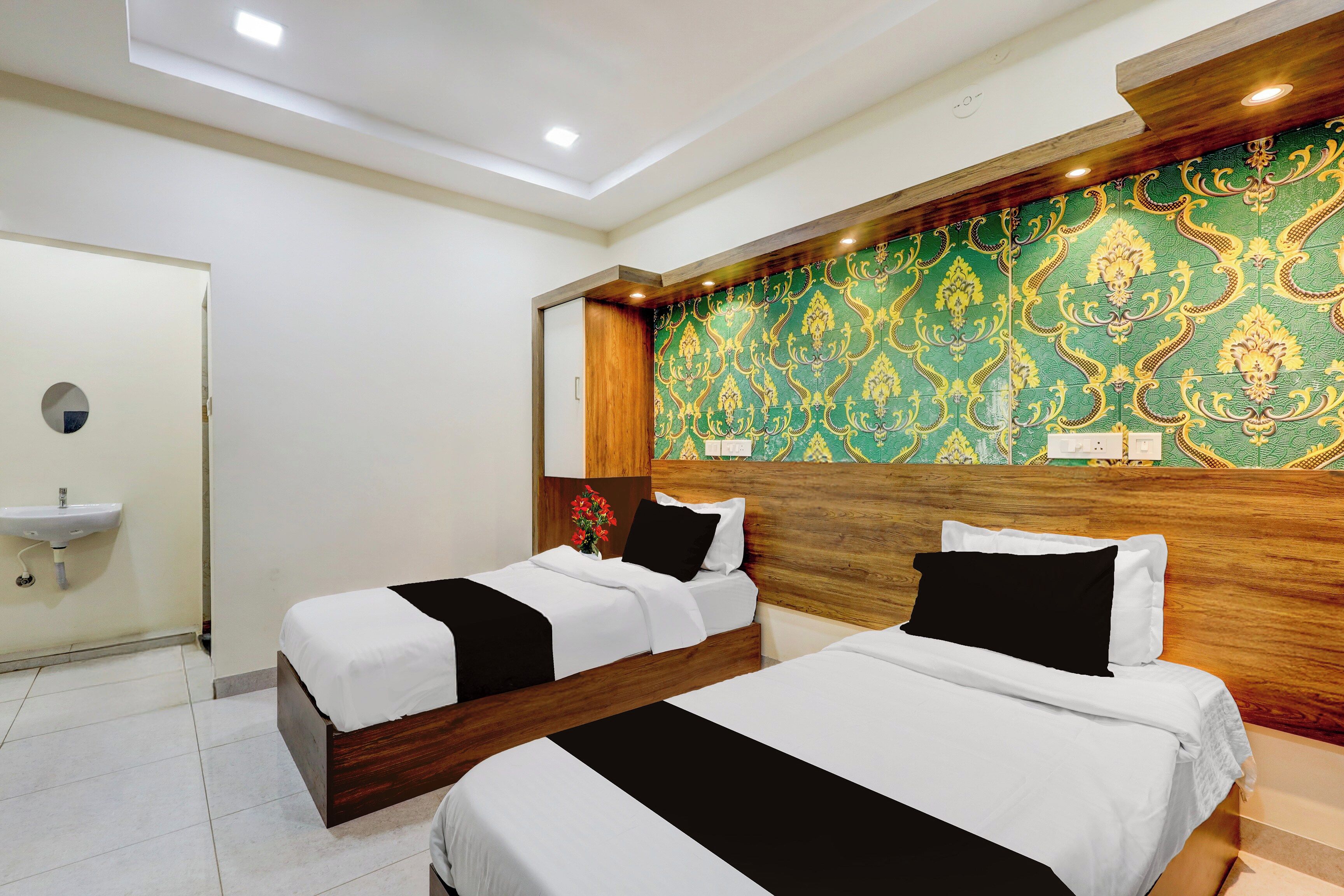 Habitación de hotel con dos camas, cabecera de madera, pared con diseño verde y lavamanos blanco.