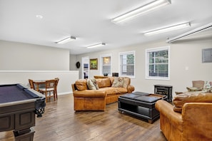A spacious living room with a pool table, leather sofas, and a fireplace. - Game Room + Covered Decks + Fire Pit • Near Lake Arrowhead | Wooded Wonder (Lake Arrowhead)
