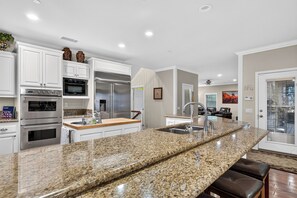 A modern kitchen with granite countertops, stainless steel appliances, and a large island. - Game Room + Covered Decks + Fire Pit • Near Lake Arrowhead | Wooded Wonder (Lake Arrowhead)