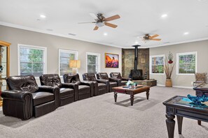A spacious living room with leather sofas, a fireplace, and a ceiling fan. - Game Room + Covered Decks + Fire Pit • Near Lake Arrowhead | Wooded Wonder (Lake Arrowhead)