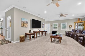 A spacious living room with a flat-screen TV, a ceiling fan, and a leather couch. - Game Room + Covered Decks + Fire Pit • Near Lake Arrowhead | Wooded Wonder (Lake Arrowhead)