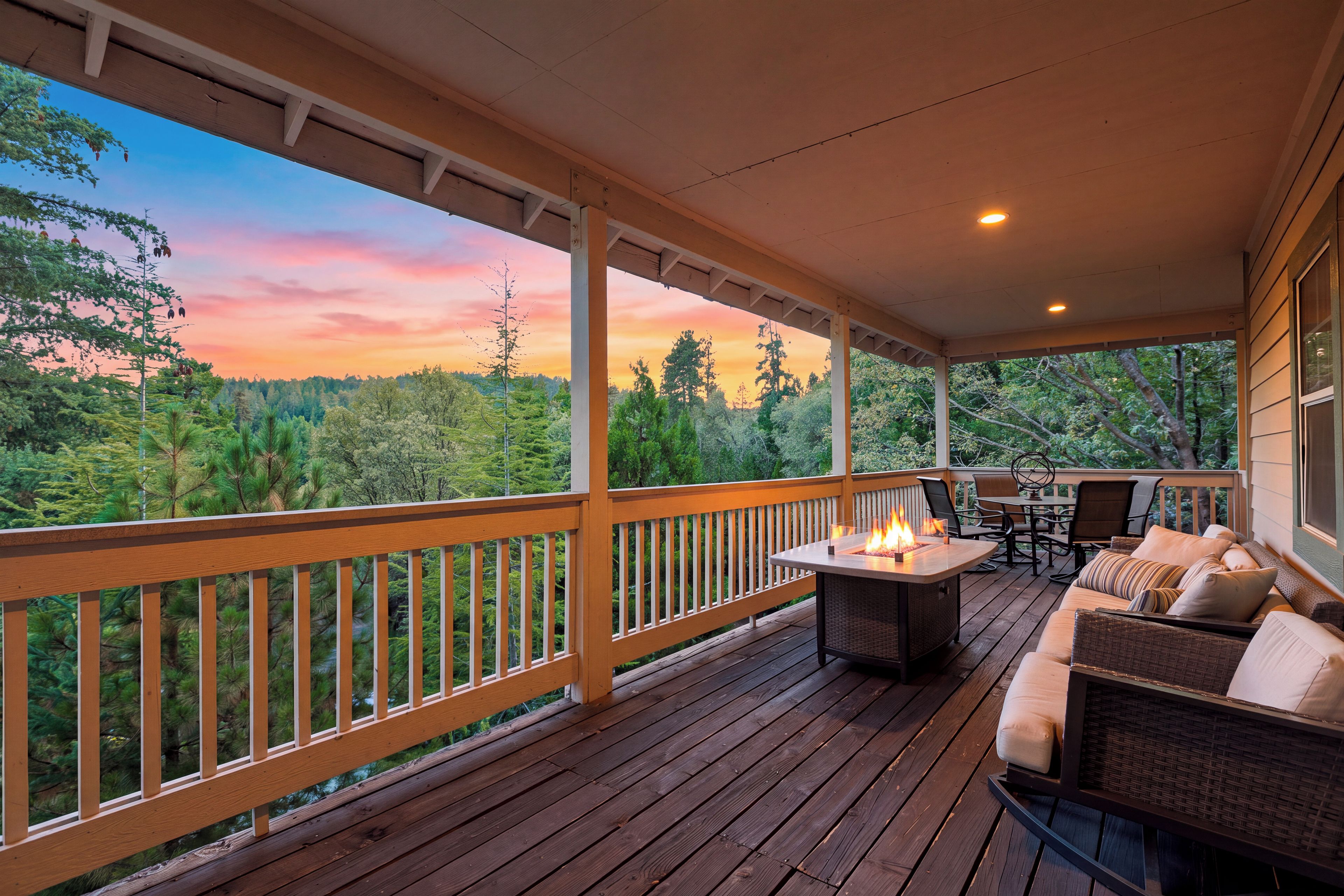 A covered outdoor deck with a fire feature, seating, and a view of the forest.
