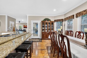 A spacious kitchen with a granite countertop, a dining area with wooden chairs, and a view through a glass door. - Game Room + Covered Decks + Fire Pit • Near Lake Arrowhead | Wooded Wonder (Lake Arrowhead)