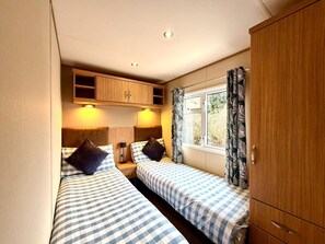 A compact room with two beds, wooden cabinets, a window with curtains, and a headboard.