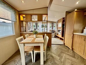 A dining area with a wooden table and chairs, a kitchen area with wooden cabinets, and a view through a window.