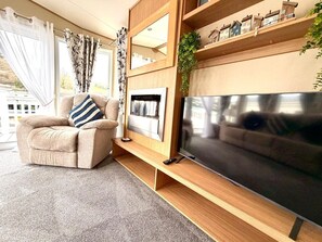 A living room with a sofa, a TV, a fireplace, and a window with curtains. - The Windermere - Luxury Retreat by the Sea in Devon (Challaborough)