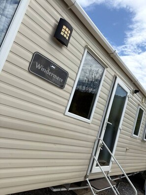 A mobile home with a sign that reads 'Windermere' and a window with a view of trees.