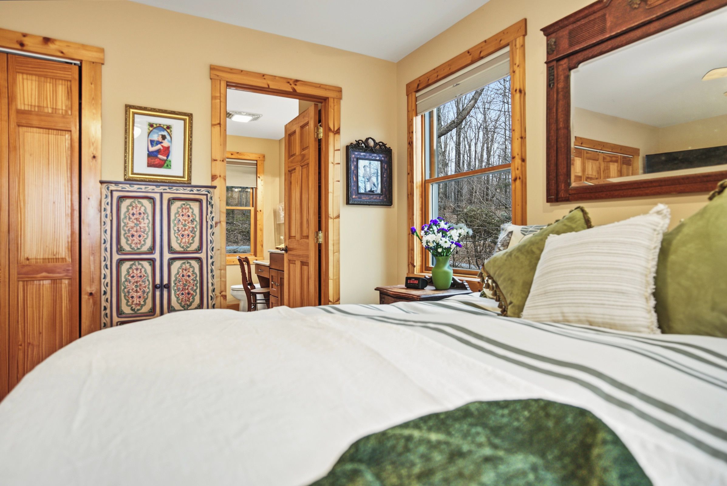 A bedroom with a bed, a dresser, a chair, a desk, and a window with a view of trees.