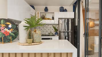 Una cocina moderna con una isla central, muebles blancos, jarrones decorativos y un refrigerador de acero inoxidable.