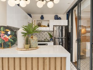 A modern kitchen with a central island, white cabinetry, decorative vases, and a stainless steel refrigerator. - The Leaf Eco Villa (Vy Da)