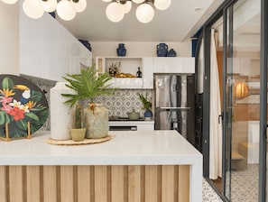 Una cocina moderna con una isla central, muebles blancos, jarrones decorativos y un refrigerador de acero inoxidable.