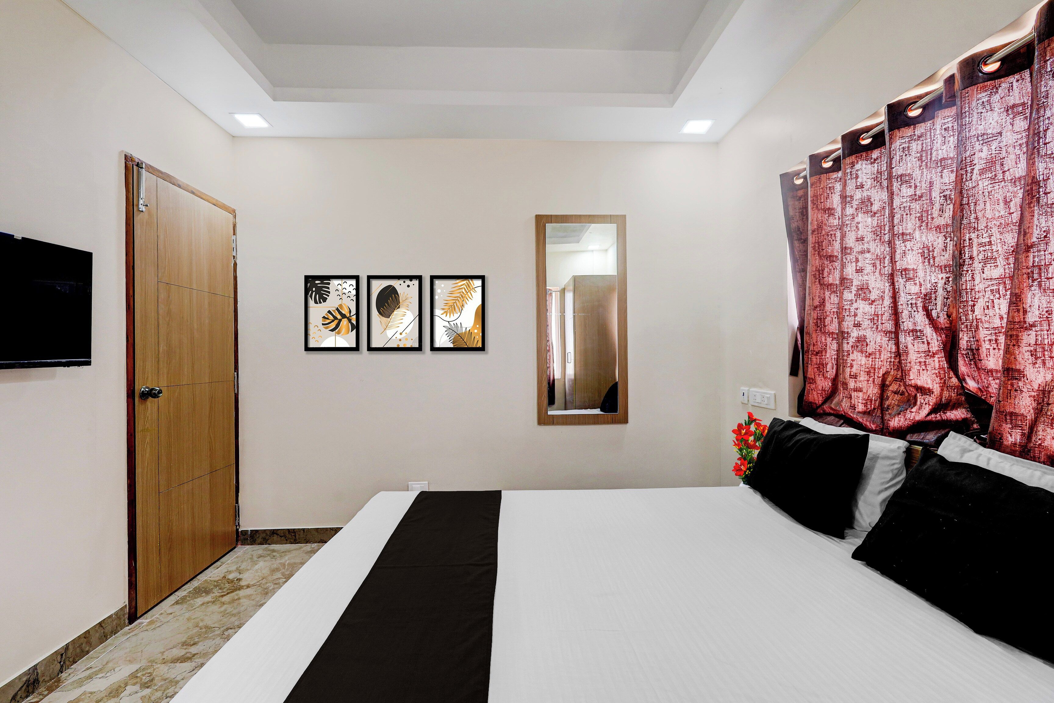 Una habitación de hotel con una cama, un televisor, una puerta y tres cuadros enmarcados en la pared.