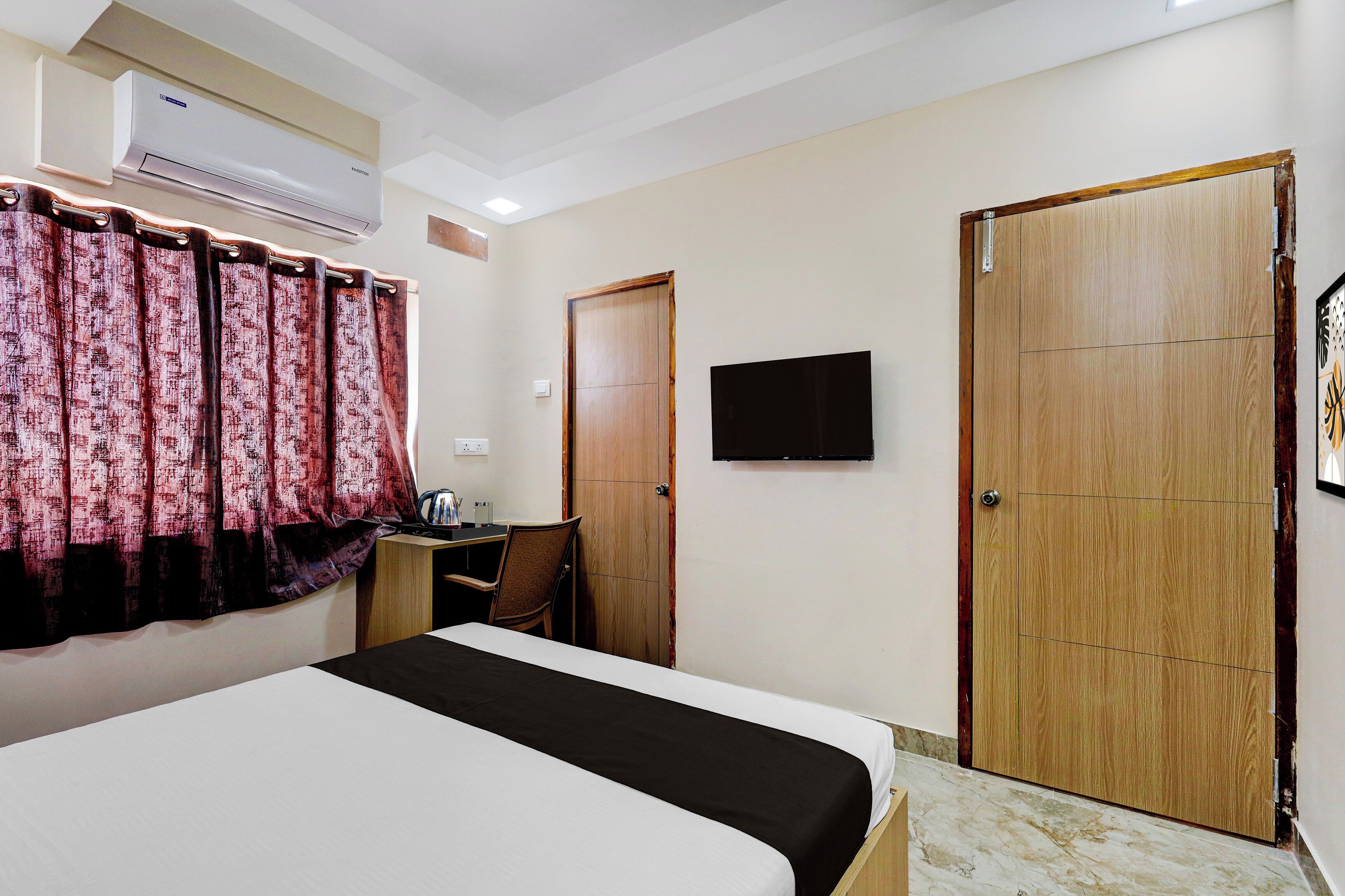 Habitación de hotel con cama, escritorio, silla, televisión y dos puertas.