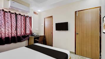 Habitación de hotel con cama, escritorio, silla, televisión y dos puertas.