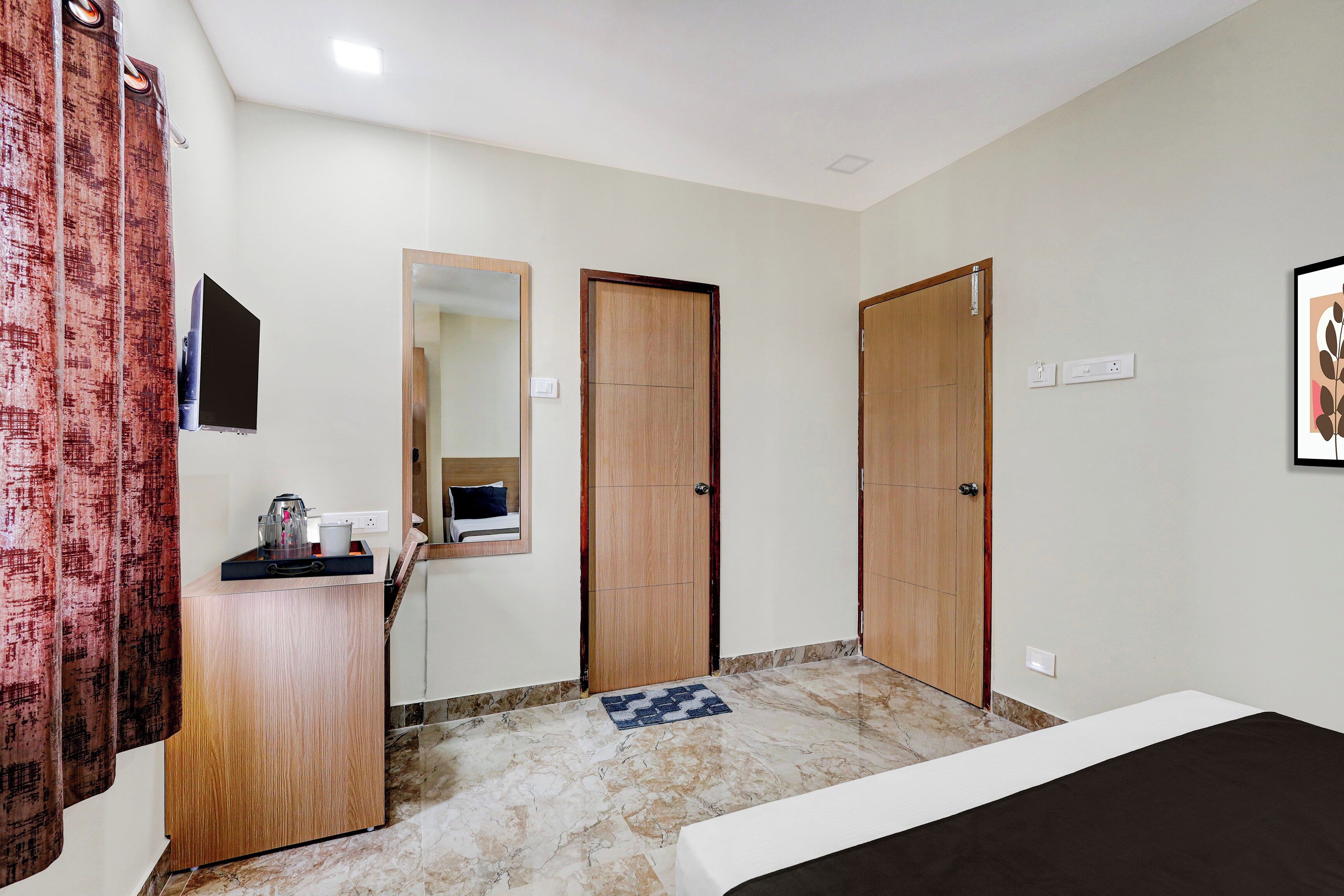 A hotel room with a bed, a wooden dresser, a mirror, and two doors.