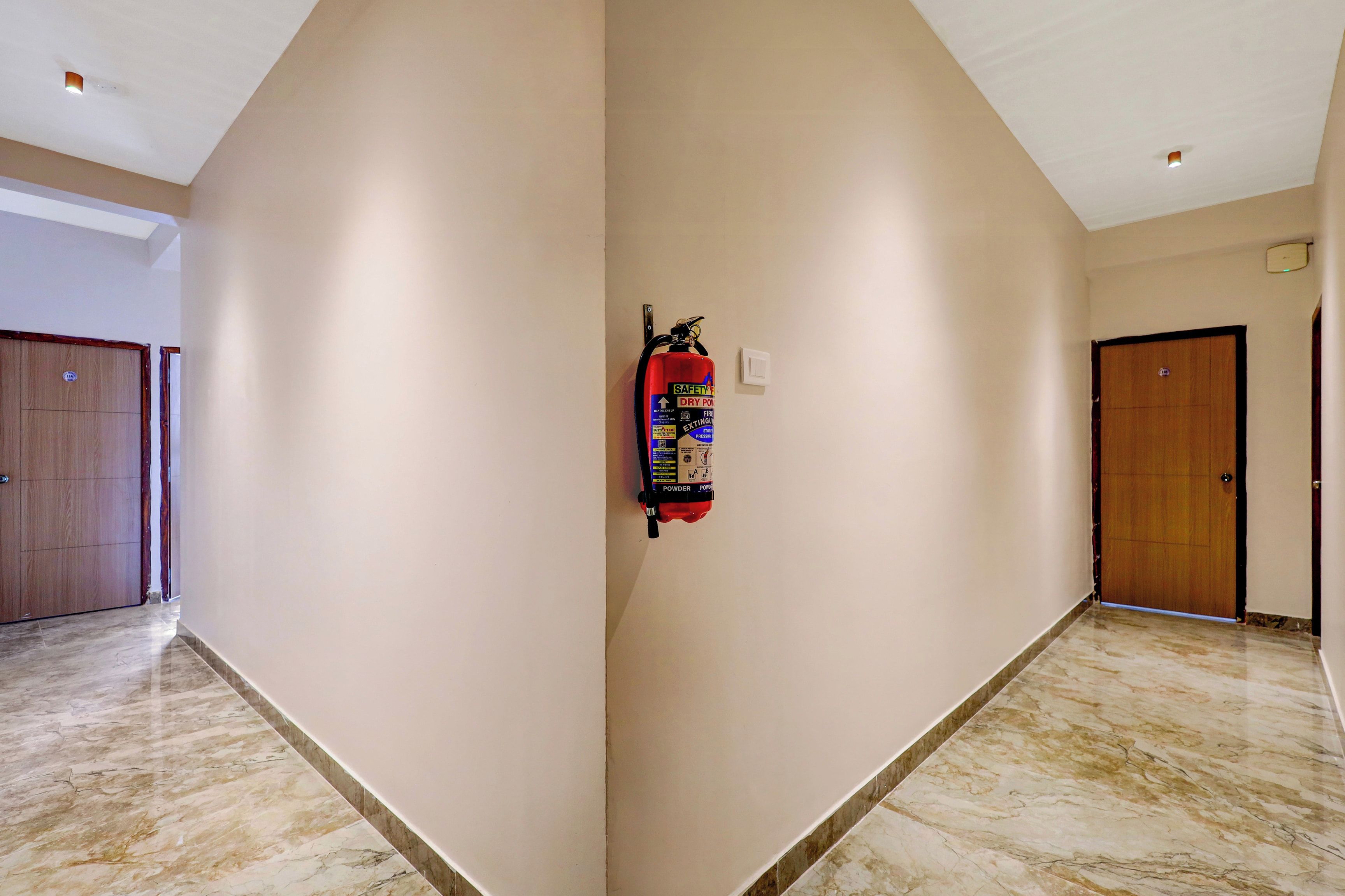 Un couloir avec un extincteur fixé au mur, une porte et un interrupteur.