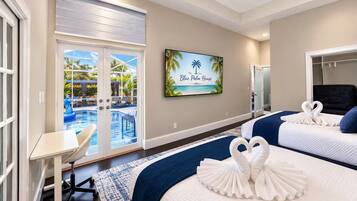 Habitación de hotel con vista a la piscina, dos camas, un escritorio y un televisor que muestra 'The Blue Palm House'.