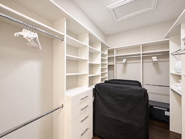 A walk-in closet with open shelving, a bed with a black cover, and a hanging rod with clothes.