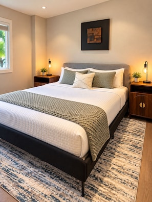 A modern bedroom with a large bed, two bedside tables, a wall-mounted artwork, and a window with blinds.
