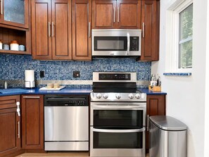 A kitchen with wooden cabinets, a stainless steel microwave, dishwasher, stove, and oven.
