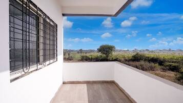 A balcony with a view of a rural landscape, white walls, and a window with metal bars.