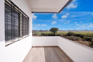 Un balcón con vista a un paisaje rural, paredes blancas y una ventana con rejas de metal.