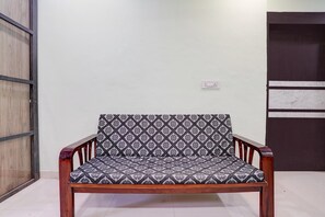 A wooden chair with a patterned cushion in a room with a white wall and a door. - Hotel O Satara Bypass (Satara)