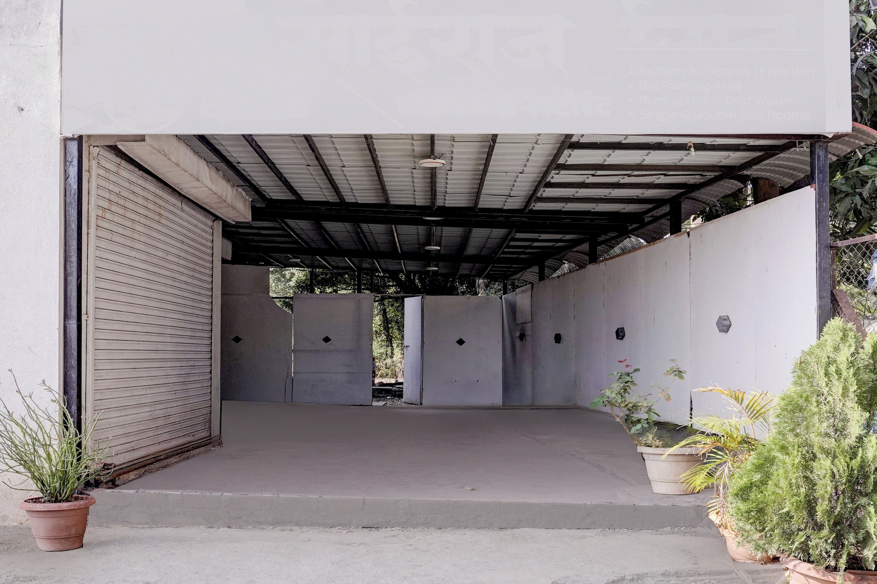 A covered outdoor area with a concrete floor, metal roof, and a closed shutter door on the left.