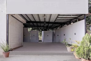 A covered outdoor area with a concrete floor, metal roof, and a closed shutter door on the left. - Hotel O Satara Bypass (Satara)