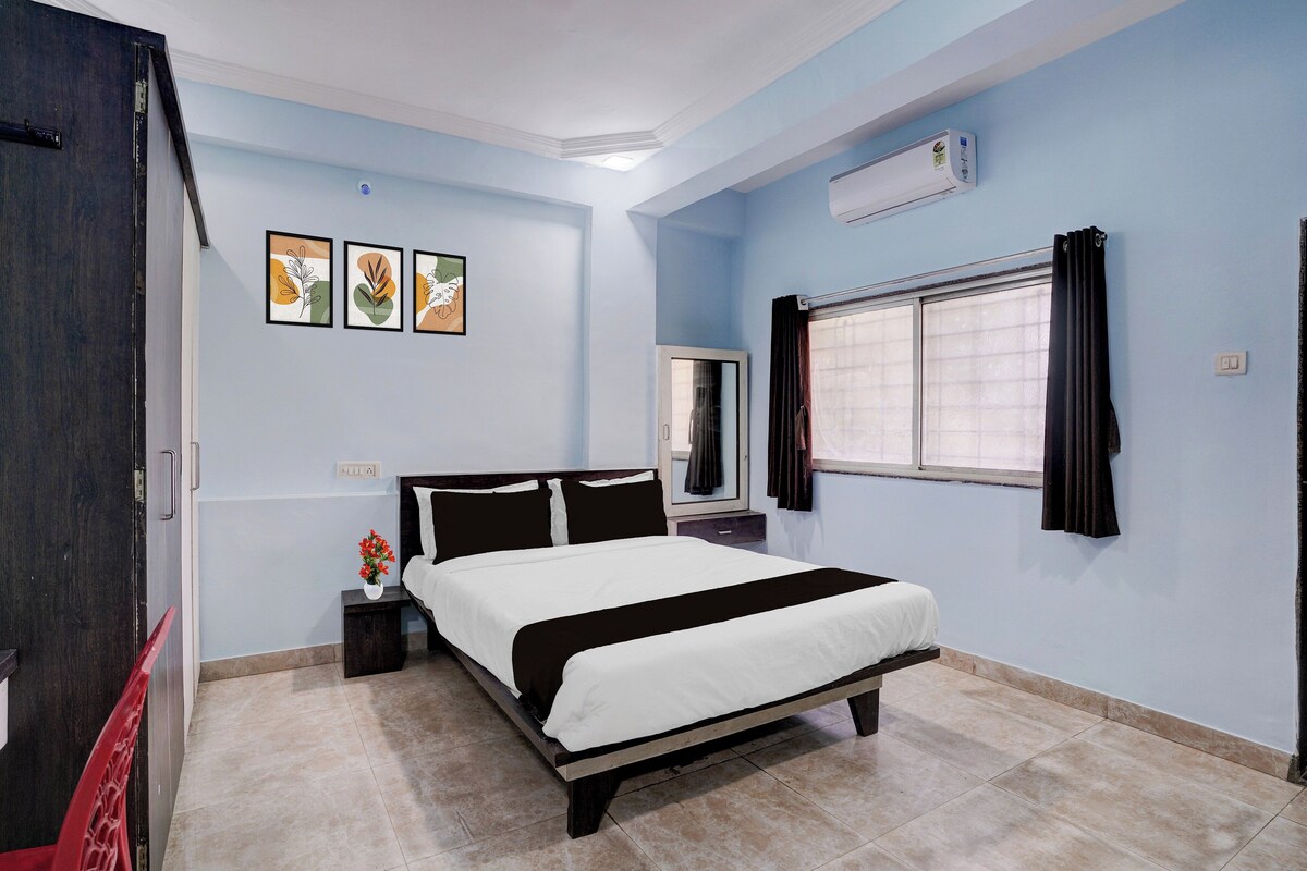 A bedroom with a bed, a nightstand, a mirror, an air conditioner, and a window with curtains.