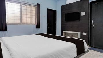 A room with a bed, a television mounted on the wall, a door, and a window with curtains.