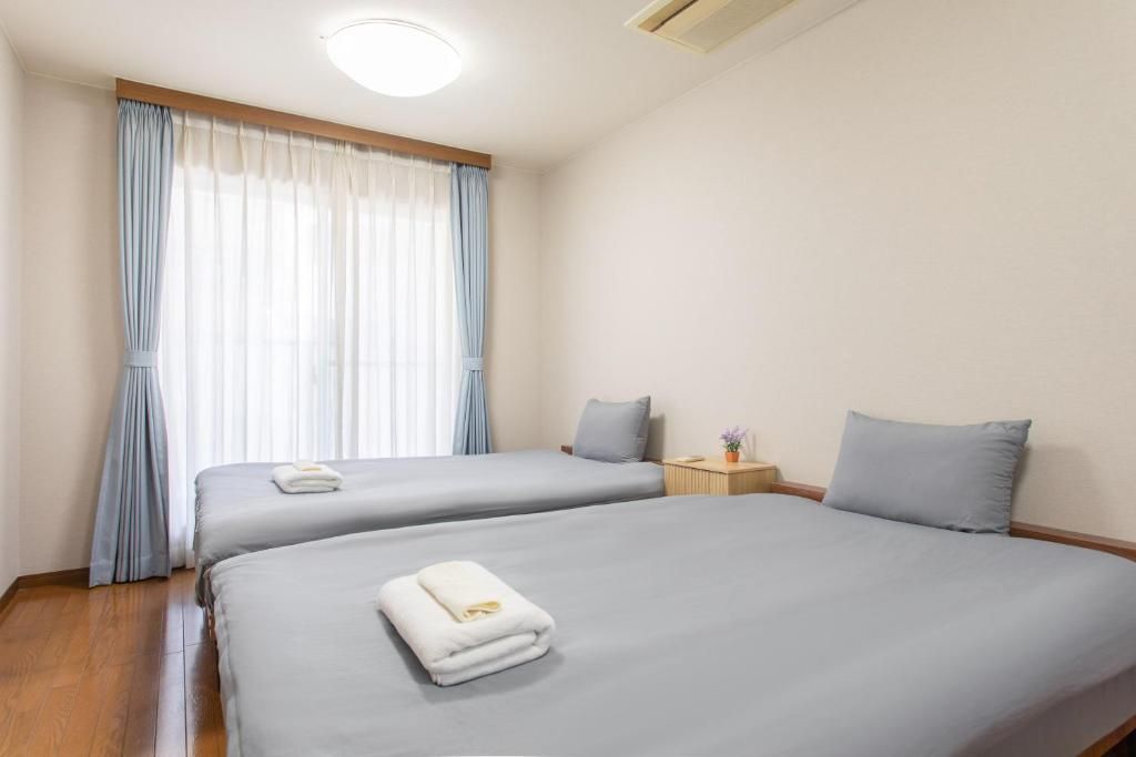 A hotel room with two beds, a bedside table with a lamp, and a window with curtains.