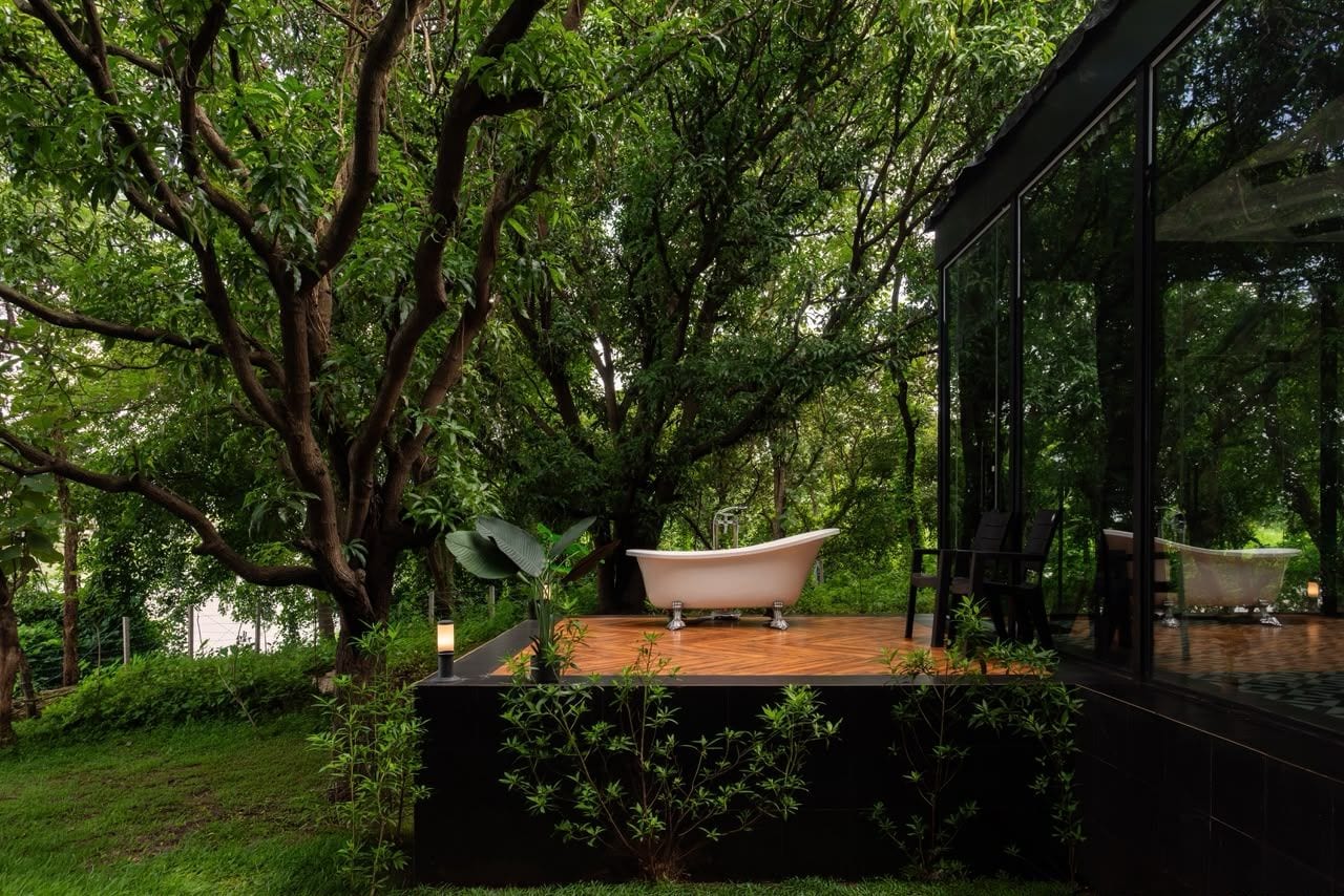 Un baño exterior moderno con una bañera independiente, rodeado de exuberante follaje y una terraza de madera.