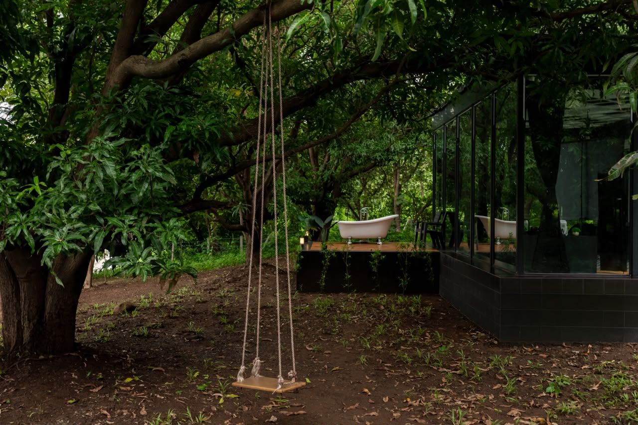 Una hamaca colgada de un árbol, una bañera sobre una plataforma y un edificio moderno con paredes de vidrio.