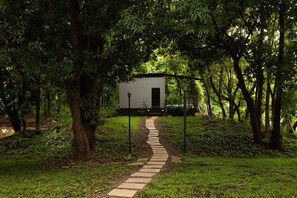 A pathway leading to a small, single-story building surrounded by dense greenery.