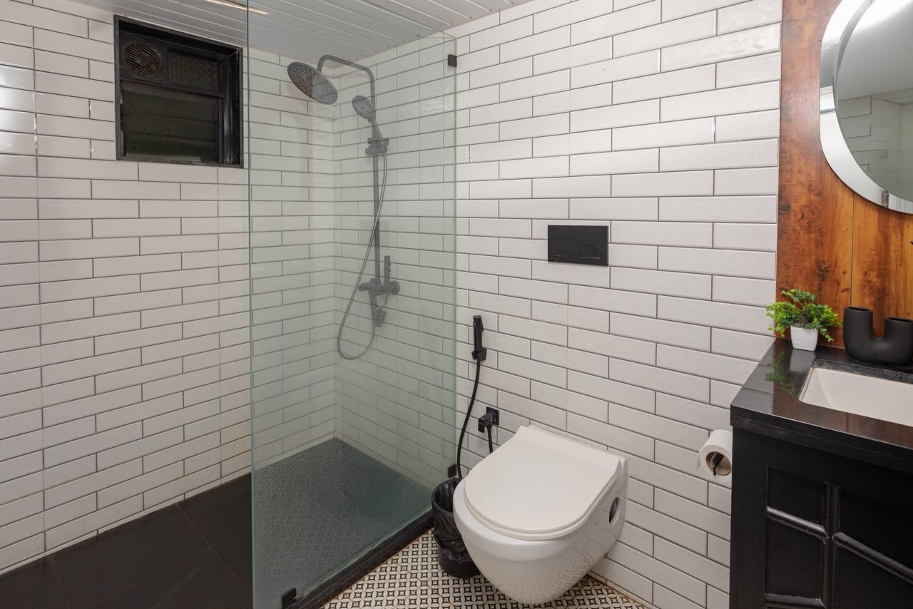 Un baño con paredes de azulejos blancos, mampara de ducha de cristal, inodoro y lavabo con encimera de madera.