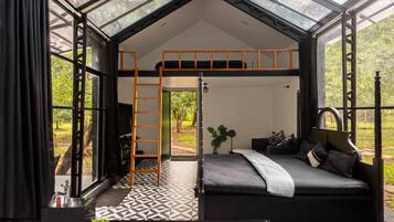 A modern bedroom with a skylight, a bunk bed, a bedside table, and a view of greenery.