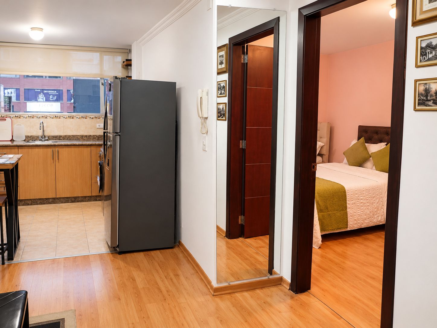 A compact living space with a kitchenette, a bed with a headboard, and a door leading to another room.