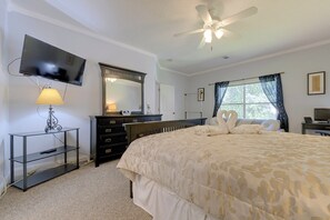 Une chambre à coucher comprenant un lit, une télévision, un bureau et un ventilateur de plafond.