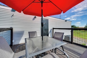 Een terras met een tafel, stoelen, een parasol en uitzicht op een wit gebouw.