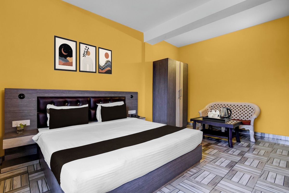 A hotel room with a large bed, a nightstand, a wardrobe, a seating area with a table, and artwork on the wall.