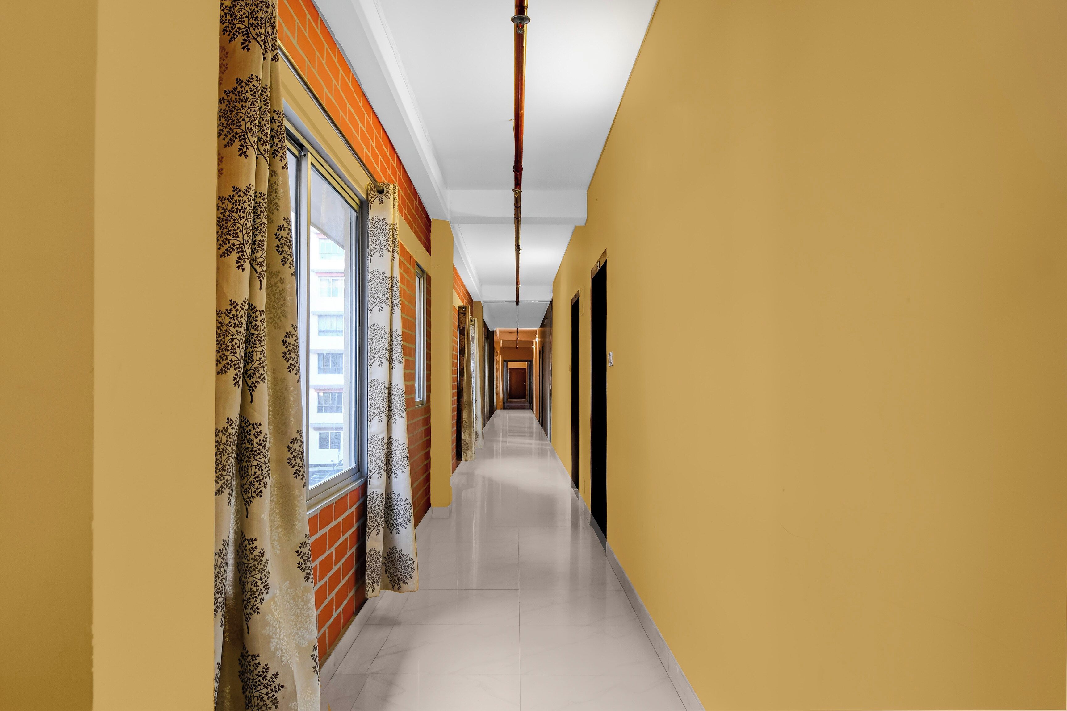 A corridor with a tiled floor, a window with a curtain, and a brick wall.